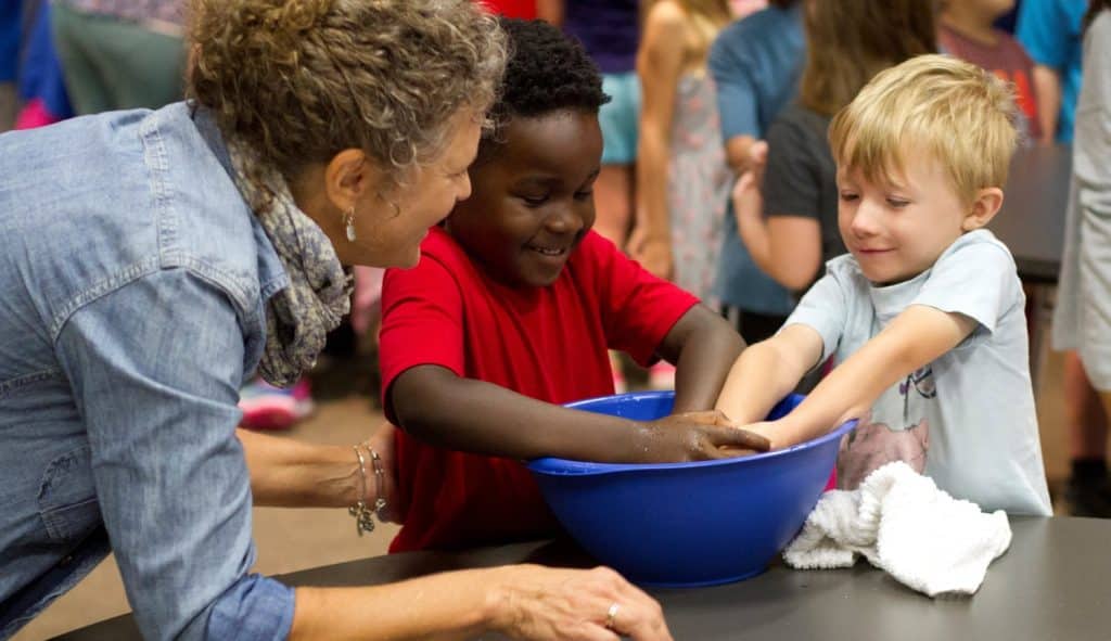 Levi Kweba and Birch Stockwell wash each other’s hands as Lynette Mast, peacebuilding
teacher, guides them, during the K-5 Gathering ceremony where students signed the pledge of nonviolence and washed hands to symbolize their care and service to and for each other. Photo by Andrew Gascho