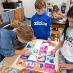 Title: Shapes CollideSize: 24”x18”Medium: fabric, acrylic paintDescription: 5th grade students began their batik creation by drawing a simple line and shape design on a small rectangle of paper and tracing it with black Sharpie. After the papers were taped onto a piece of cardboard, covered with wax paper, and finally covered with a large piece of white fabric, students carefully traced their designs with glue onto the fabric. Once the glue was dry, students painted the sections of their design with acrylic paint. When the paint was dry, the glue was washed out of the fabric to reveal the white outline left by the glue. As the final step in their creative process, the class brainstormed title ideas for their piece then voted for their favorite.