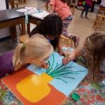 Title: Mary Jo’s Flower FarmSize: 18” x 24”Medium: acrylic paint, acetate paperDescription:  Inspired by their field trip with kindergarten science buddies to Mary Jo’s Flower Farm, each second grade artist designed a colorful flower using acetate paper. Students worked in small groups to paint a foreground, background, and vase. After painting individual stems, students attached their flowers to the composition. As the final step in their creative process, the class brainstormed title ideas for their piece then voted for their favorite.