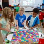 Title: Rainbow ShadowsSize: 24”x18”Media: paper, acrylic paintDescription: 3rd grade artists each painted four 4x4 squares of paper a solid background color (chosen from the project color scheme), then used a variety of tools such as spools, wooden blocks, and lids to create patterns and implied textures. The large squares were cut into a series of squares and rectangles. Students adhered their individual pieces onto a cradled wooden panel, intermingled with those of their classmates, arranging them into a quilt pattern. As the final step in their creative process, the class brainstormed title ideas for their piece then voted for their favorite.